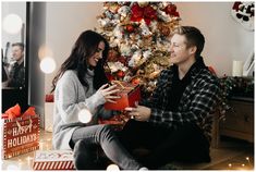 a man and woman sitting in front of a christmas tree with presents under the tree