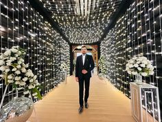 a man in a tuxedo is walking down a hall decorated with lights and flowers