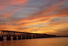 the sun is setting behind a bridge over water