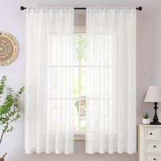 a window with white sheer curtains and a plant in front of it on a dresser