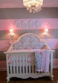 a baby crib in a room with pink and gray striped walls, chandelier and lights