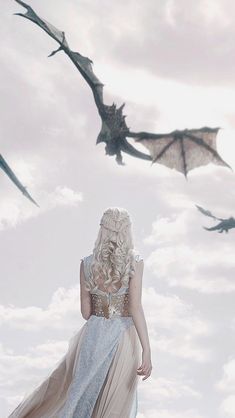 a woman standing in front of two flying dragon shaped kites on a cloudy day