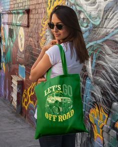 a woman is holding a green bag in front of a wall with graffiti on it