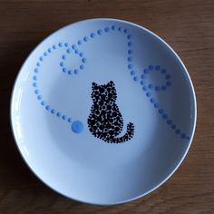 a white bowl with a black cat drawn on the side and blue dots around it