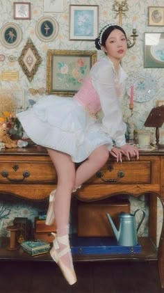 a woman in white dress sitting on top of a wooden table next to a dresser