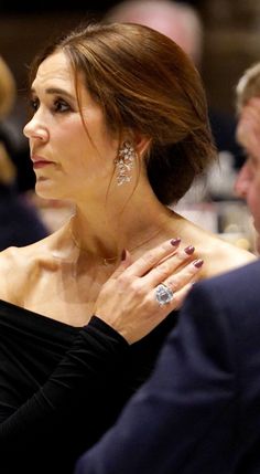 a woman in a black dress with her hand on her chest and wearing diamond rings