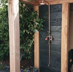 an outdoor shower in the corner of a wooden structure with plants growing out of it