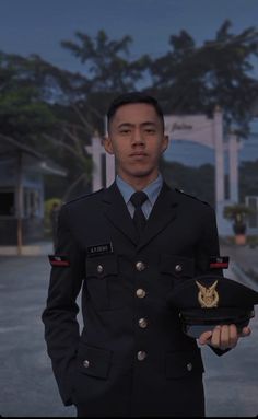 a man in uniform holding a hat and wearing a badge on his left hand, with trees in the background