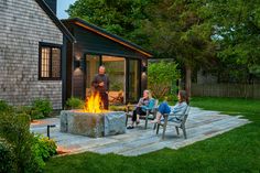 three people sitting around a fire pit in the backyard