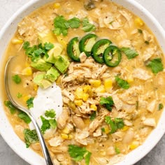 a white bowl filled with chicken, corn and avocado soup next to a spoon