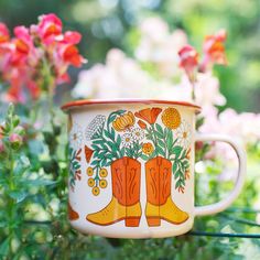 an orange and white coffee cup with boots on it sitting in front of some flowers