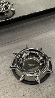 a dog bowl with spikes on the bottom is shown in front of a mirror and another metal object behind it