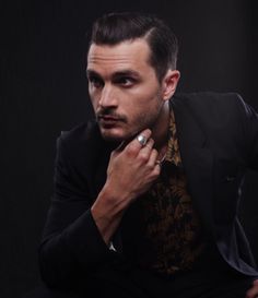 a man with a ring on his finger sitting in front of a black background wearing a suit