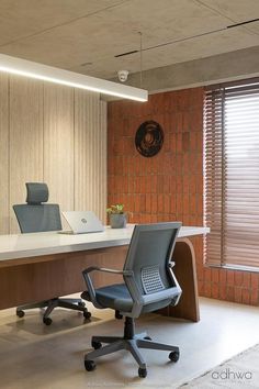 an office with a desk, chair and laptop on top of the desk in front of a brick wall