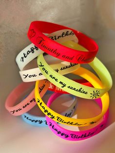 several bracelets with words written on them in different colors and font, all stacked together