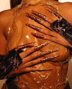 a woman with her hands on her chest covered in gold nail polish and black gloves