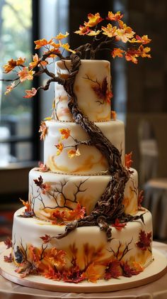 a three tiered wedding cake decorated with fall leaves and branches on a table in front of a window