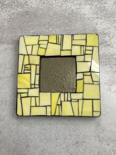 a yellow and white mosaic tile with a mirror in the center on a concrete surface