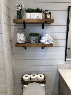 a white toilet sitting in a bathroom next to a wooden shelf filled with rolls of toilet paper