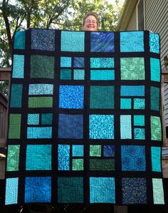 a woman holding up a blue and green quilt