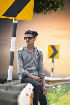 a man sitting on top of a bench next to a yellow and black street sign