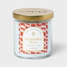 a jar of peppermint snow scented candle on a white surface with a gold lid