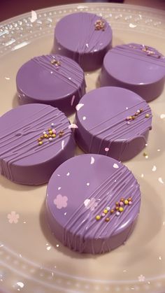 four purple desserts sitting on top of a white plate with confetti sprinkles