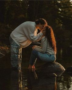 a man kneeling down next to a woman on top of a rock in the water