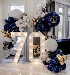 balloons and lights are arranged in the shape of an seventyth birthday sign with white, gold and blue balloons