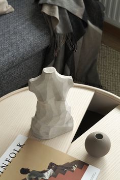 a white vase sitting on top of a wooden table next to a book and magazine