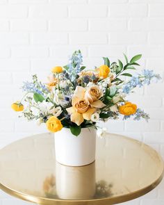 a white vase filled with yellow flowers on top of a gold table next to a brick wall