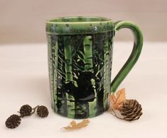 a green and black coffee mug sitting next to some pine cones