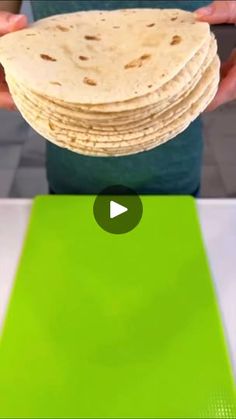 a person holding a stack of tortilla on top of a green cutting board