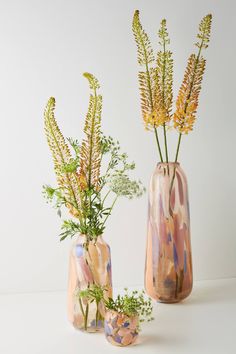 two vases with flowers in them sitting on a white counter top next to each other