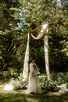 a woman in a white dress standing under a canopy with flowers and greenery around her