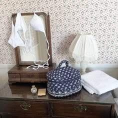 a mirror, lamp and other items are on a dresser in a room with floral wallpaper