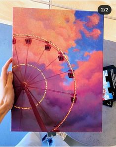 someone is painting a ferris wheel in the sky with pink and blue clouds behind it