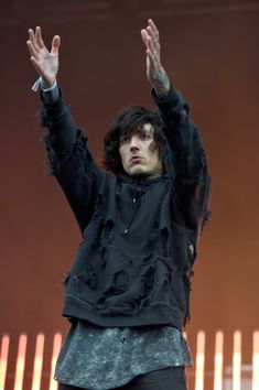 a man with his hands in the air at a music festival, wearing all black