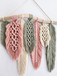 four different colored feathers hanging from a wooden stick on a white wall with some string attached to it