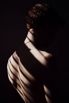 the shadow of a man's back and neck is cast on his shirtless body