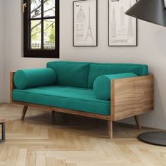 a green couch sitting in front of a window next to a wooden table and lamp