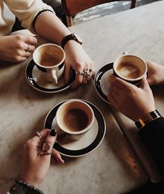 three people sitting at a table with cups of coffee in front of them, holding hands