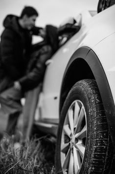 a man standing next to a white car on top of a grass covered field,