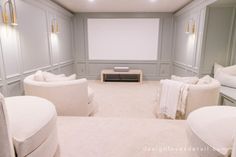 an empty room with white furniture and pillows on the couches, in front of a projector screen