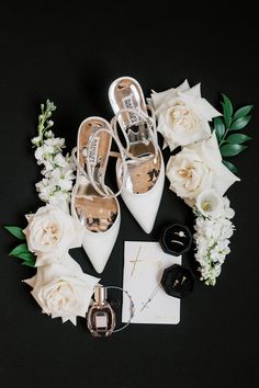 wedding shoes and accessories laid out on a black background with white flowers in the middle