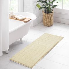 a white bath tub sitting next to a green plant in a bathroom under a window