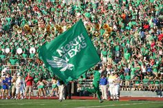 a marching band carrying a green flag in front of a large group of people on a football field