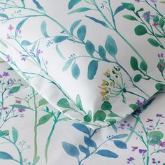 a white bed with green and purple flowers on it's pillowcase, along with two matching pillows