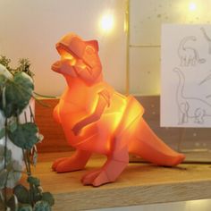 a dinosaur lamp sitting on top of a wooden table next to a potted plant