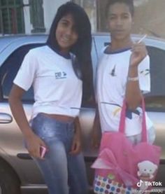 two people standing next to each other in front of a car with a pink bag